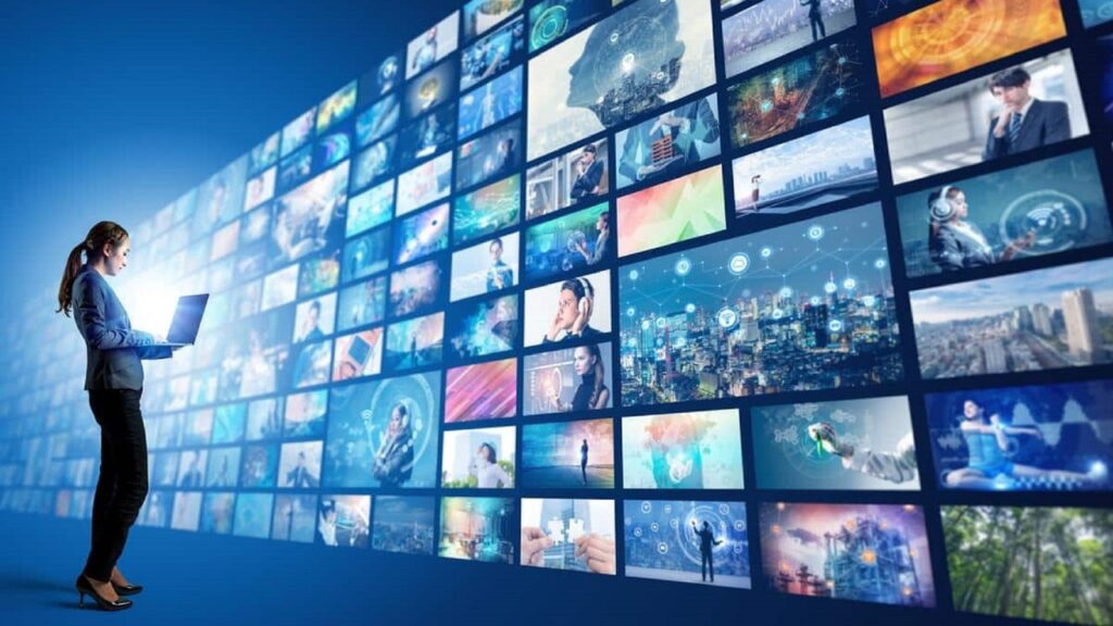 Mujer con portátil delante de pantalla enorme con cadenas de televisión